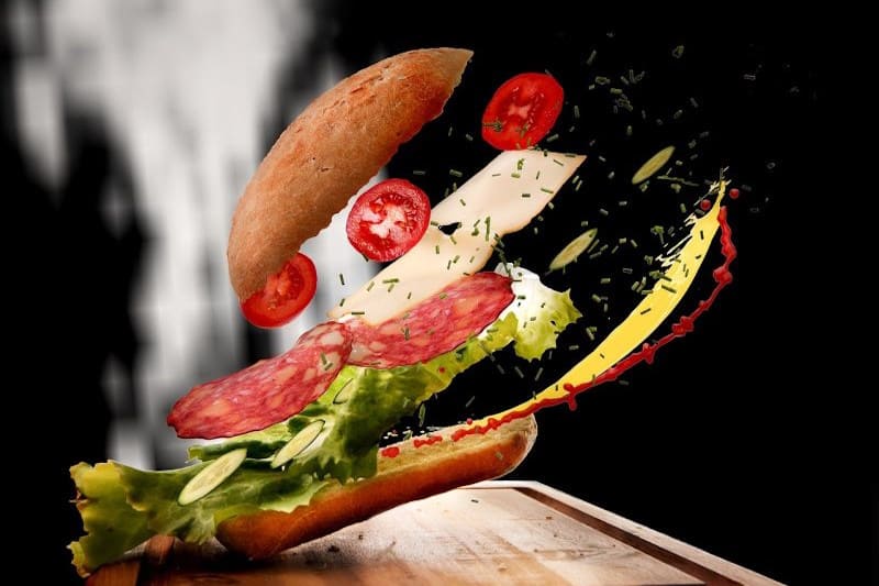 ein belegtes Baguette, mit Salat, Tomaten und Gurkenscheiben, Scheibenkäse und Salami aufgespalten in die einzelnen Kompotente