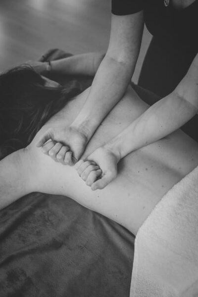 eine Frau wird liegend am Rücken von einer Therapeutin mit den Unterarmen behandelt