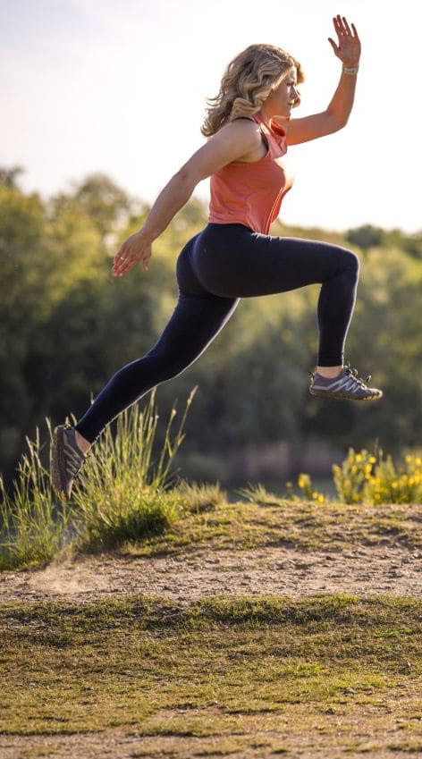 eine sportliche Frau springt im Lauf in die Luft vor dem Hintergrund einer Naturlandschaft