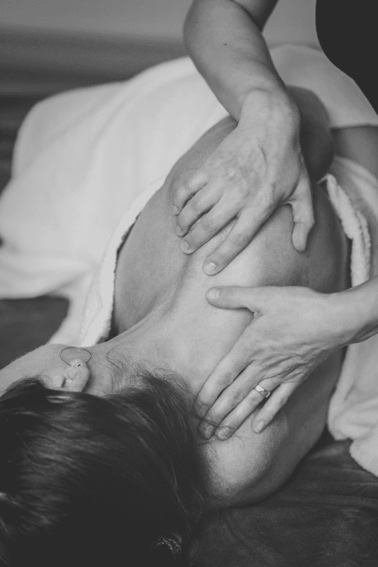 ein weibliche Person liegt seitlich auf einer Liege und wird am hinteren Nacken und Schulter mit Händen gedehnt