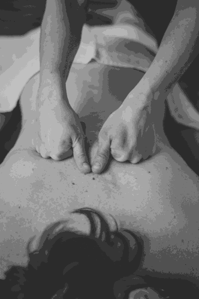 eine Frau liegt auf dem Bauch mit freiem Oberkörper und zwei zu Fäusten gefalteten händen mit aufgestellten Daumen führen über den Rücken.